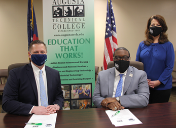 Caucasian male wearing a blue face mask, blue suit jacket, white collared shirt, light blue tie, hands folded while sitting down at a table, white paper in front of him with a green pen; African American male wearing a black Augusta Tech branded face mask, light gray suit, silver Augusta Tech lapel pin, white collared shirt, blue/purple tie, silver watch, hands folded white sitting at a brown table, white papers on brown table in front of him with a green pen; Caucasian female standing wearing a black Augusta Tech branded face mask, blue shirt, hands folded together, black pants, background features an American flag, the state of Georgia flag, large retractable banner showing old Augusta Tech logo, verbiage reads: www.augustatech.edu, Education That Works; bulleted list reads Allied Health Sciences and Nursing, Business and Personal Services, and Engineering Technology, Industrial Technology, and Learning Support, photos underneath the bulleted list.