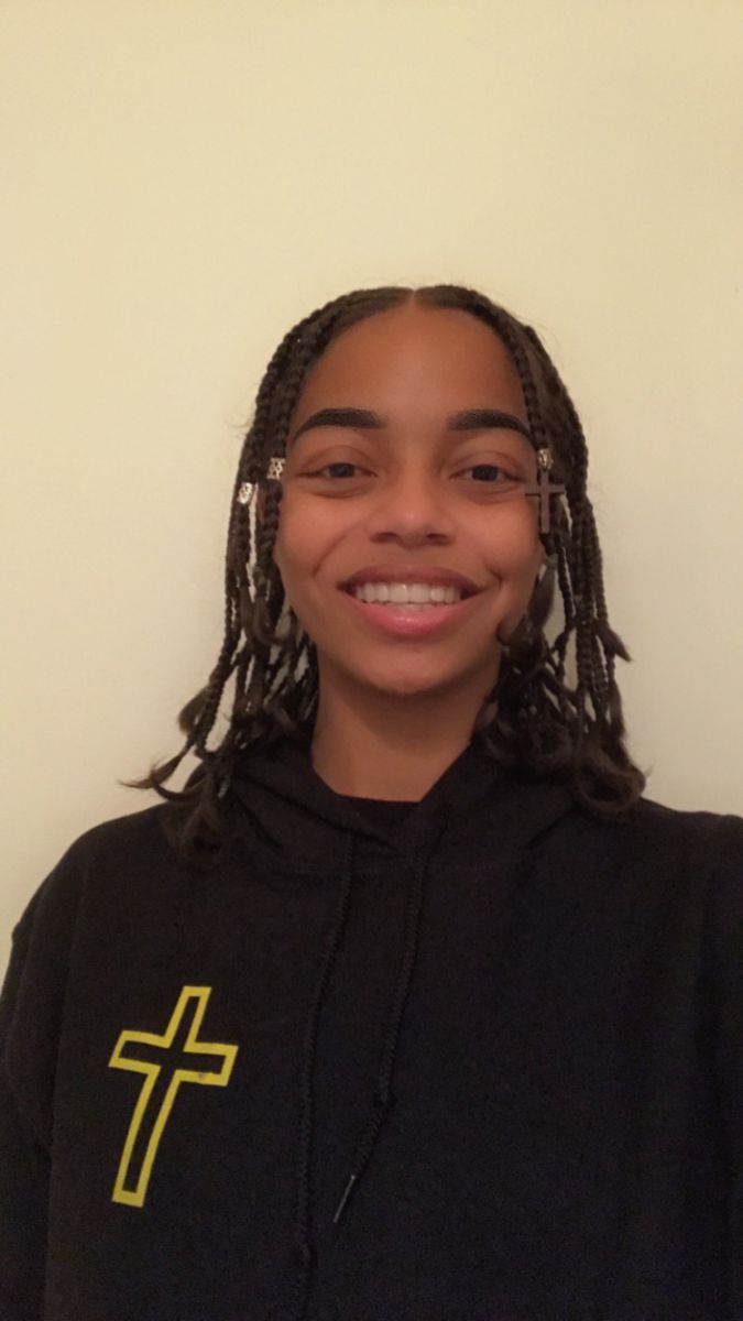 Smiling African American girl; hair in braids with hair jewelry; wearing a black sweatshirt with a picture of a gold cross.