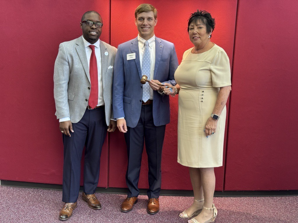 President Jermaine Whirl, Mr. Nic Woods, and Ms. Pat Woods stand together pictured against a red backdrop.