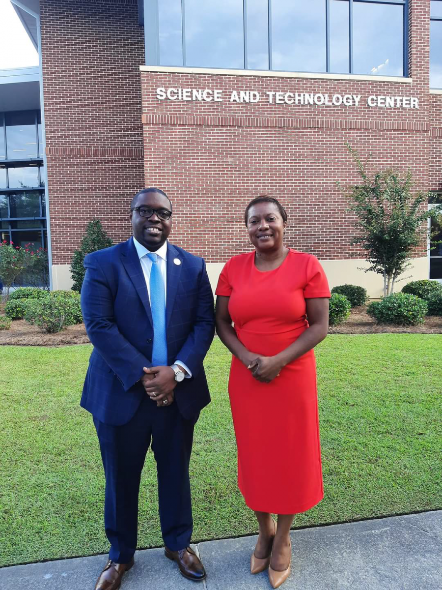 Dr. Jermaine Whirl, an African American male smiles wearing black rimmed glasses, a navy suit with a light blue tie and white shirt beside Kimberly Ballard-Washington, J.D., an African American Female, who is also smiling wearing a red dress. The two stand in front of the Science and Technology Center