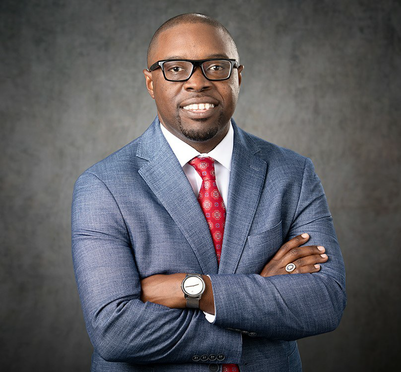 Dr. Jermaine Whirl, an African American male and President of Augusta Technical College, smiles wearing a light blue suit jacket, white collared shirt and red tie with black squre rimmed glasses.